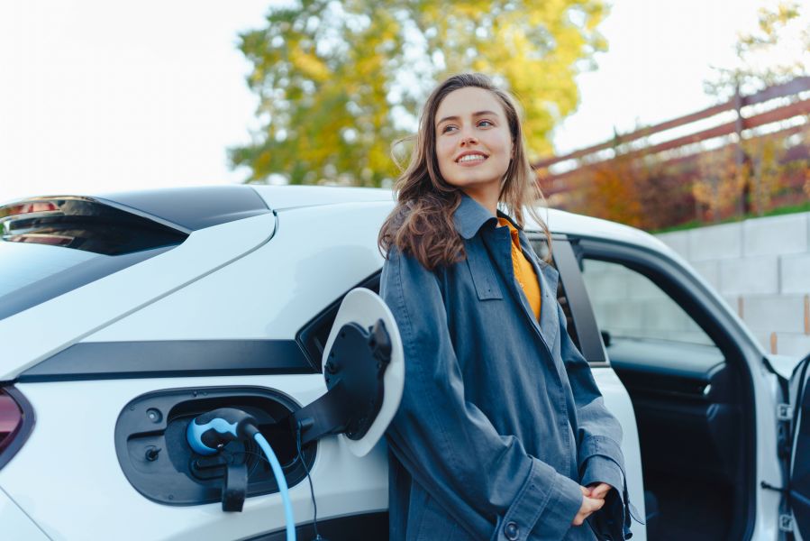 Mulher jovem satisfeita aguardando o seu carro elétrico carregar - Adobe