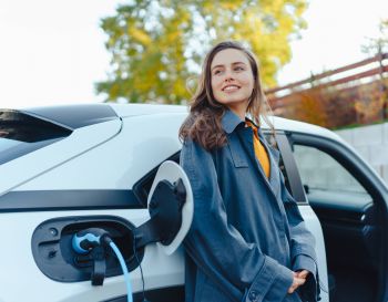 Mulher jovem satisfeita aguardando o seu carro elétrico carregar - Adobe
